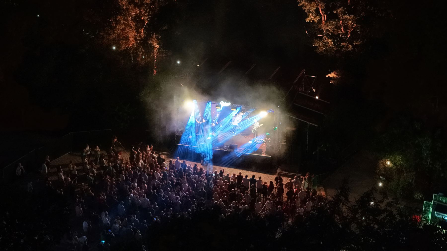 Aerial shot looking down on the Strings Festival stage with blue beam lighting cutting through haze, audience gathered in front