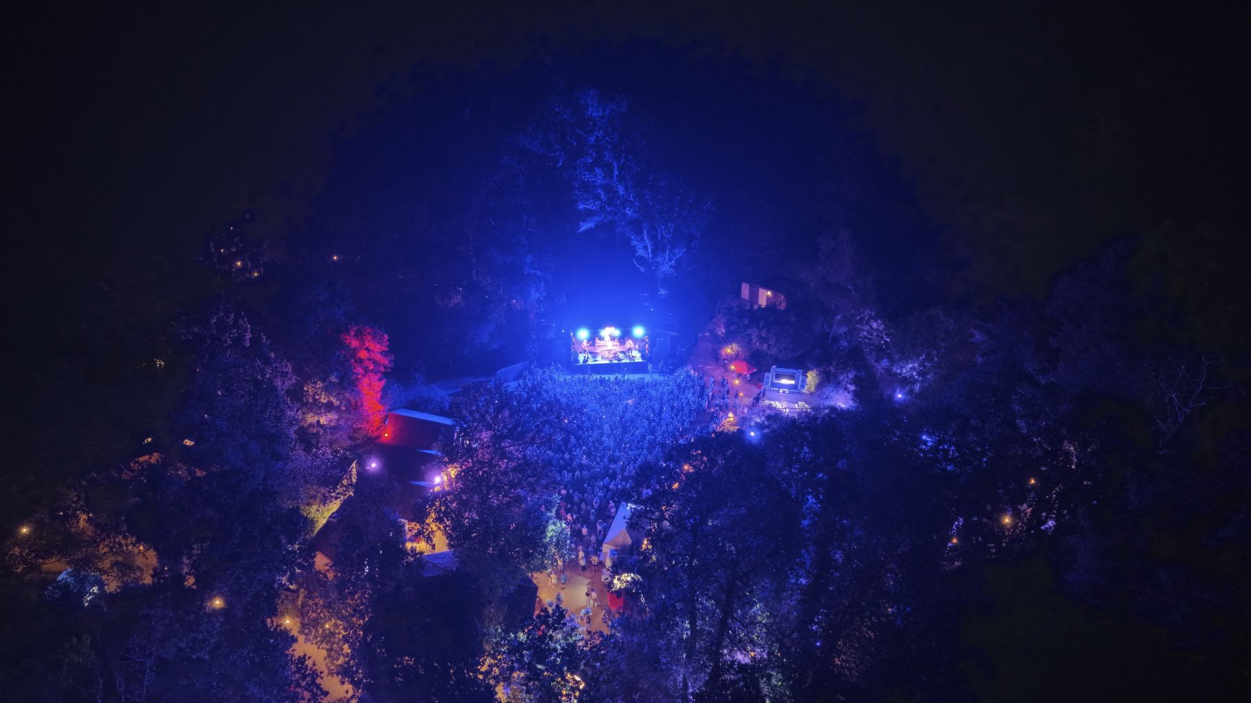 Wide aerial view of The Woodland Venue at Robin Hill washed in blue stage light at night